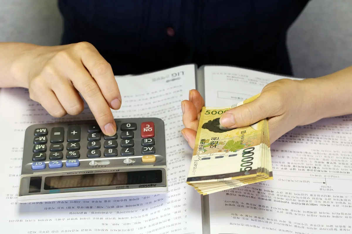 Main anonyme ouvrant un dossier d'épargne avec calculatrice et papiers sur une table